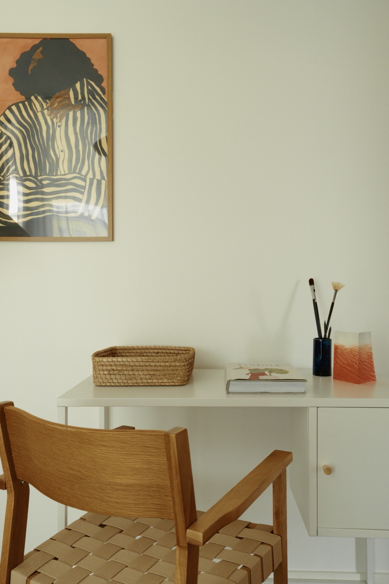 A quiet work corner: a wooden chair, a desk and a framed print on a pale wall